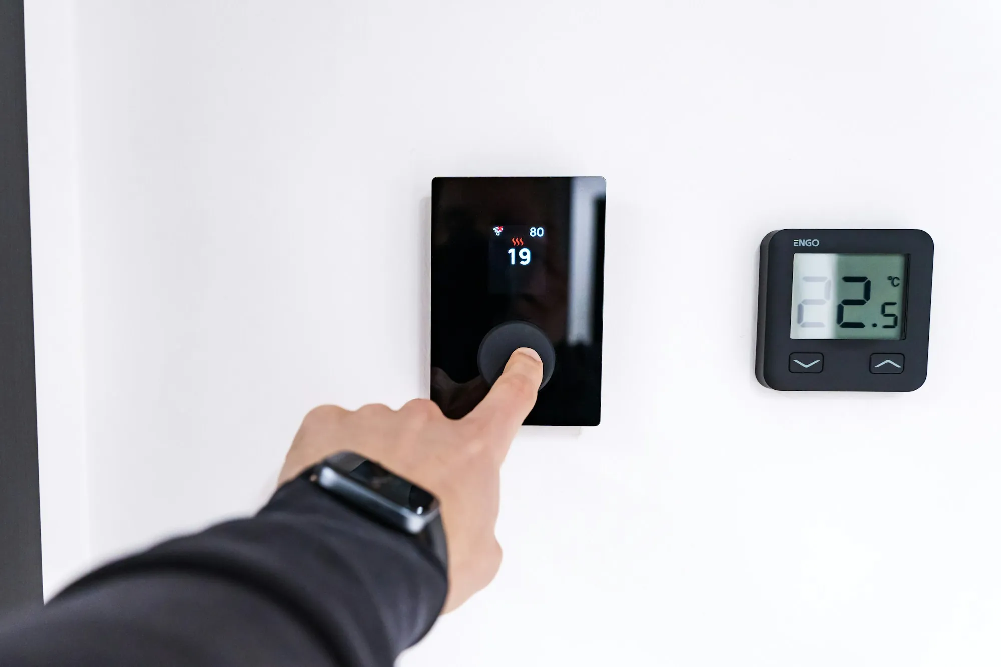 Hand pressing the dial of a smart thermostat on a wall